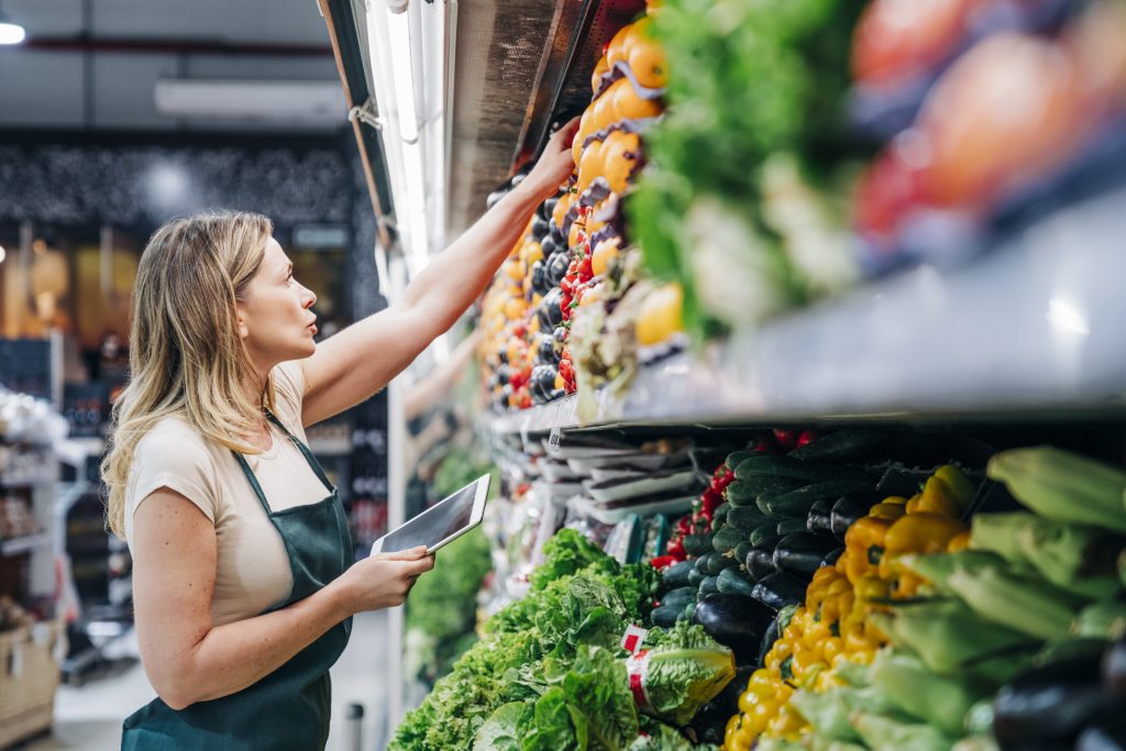 A grocery store employee working in the vegetable section